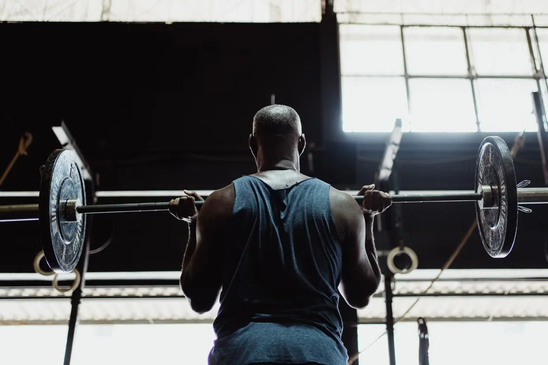 A weightlifter sets up with a loaded barbell across his shoulders in a gym.
